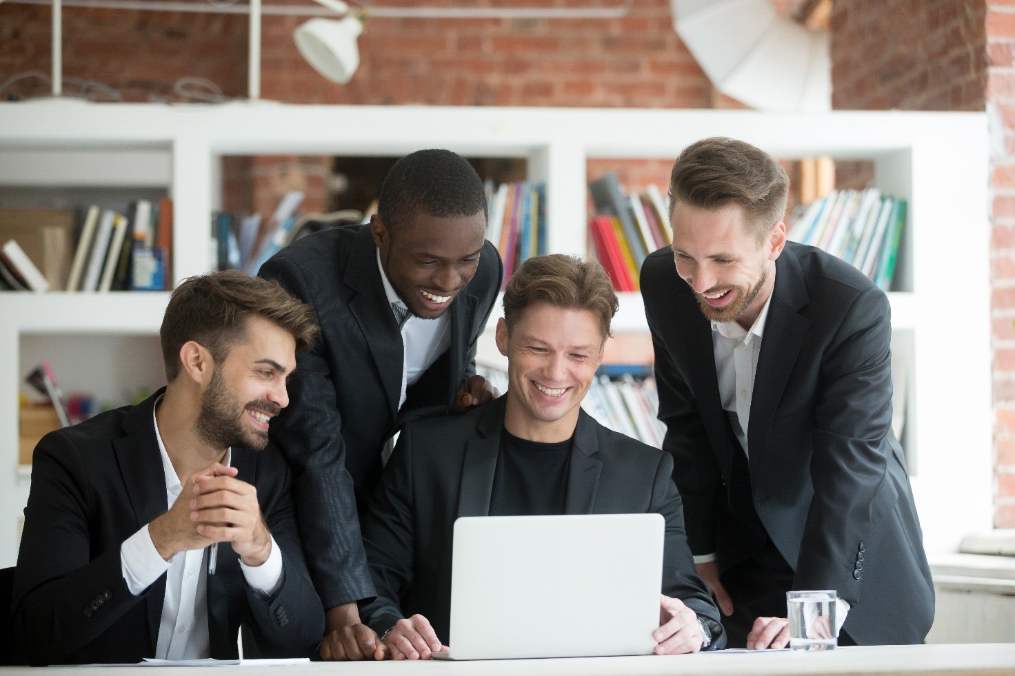 quattro rappresentanti di vendita vestiti con completo nero e camicia bianca guardano un computer e sorridono