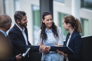 ad un appuntamento di lavoro due persone si stringono la mano mentre la donna che li ha presentati li guarda e sorride