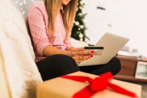 donna con in mano una carta di credito fa acquisti online seduta sul divano a Natale